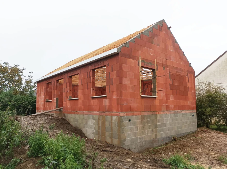 Garage neuf avec deux portes sectionnelles blanches et fenêtre rectangulaire, situé sur terrain gravillonné