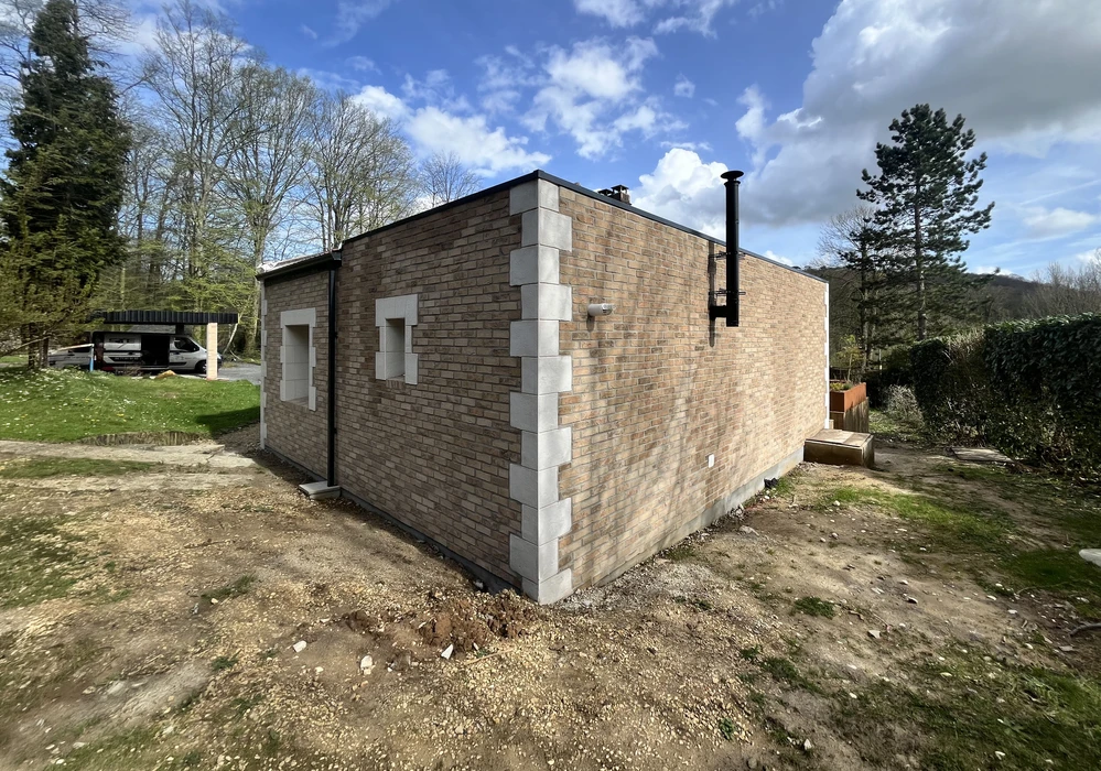 Chantier de construction résidentielle en cours, maison individuelle avec murs en briques rouge-orangé partiellement achevée
