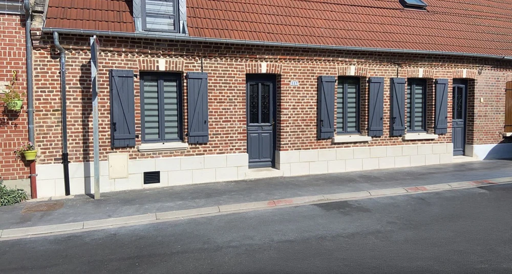 Façade de maison traditionnelle en briques rouges avec volets battants gris anthracite, porte d'entrée assortie et fenêtres à persiennes