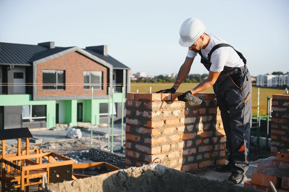 Personne dessinant un plan architectural sur papier blanc, main tenant un crayon rouge traçant des lignes de construction