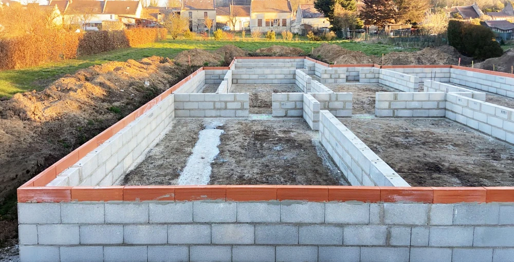 Chantier de construction résidentielle en cours, maison individuelle avec murs en briques rouge-orangé partiellement achevée