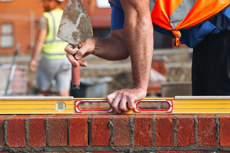 Chantier de construction résidentielle avec ouvriers miniatures travaillant sur une maison à ossature bois en cours d'édification